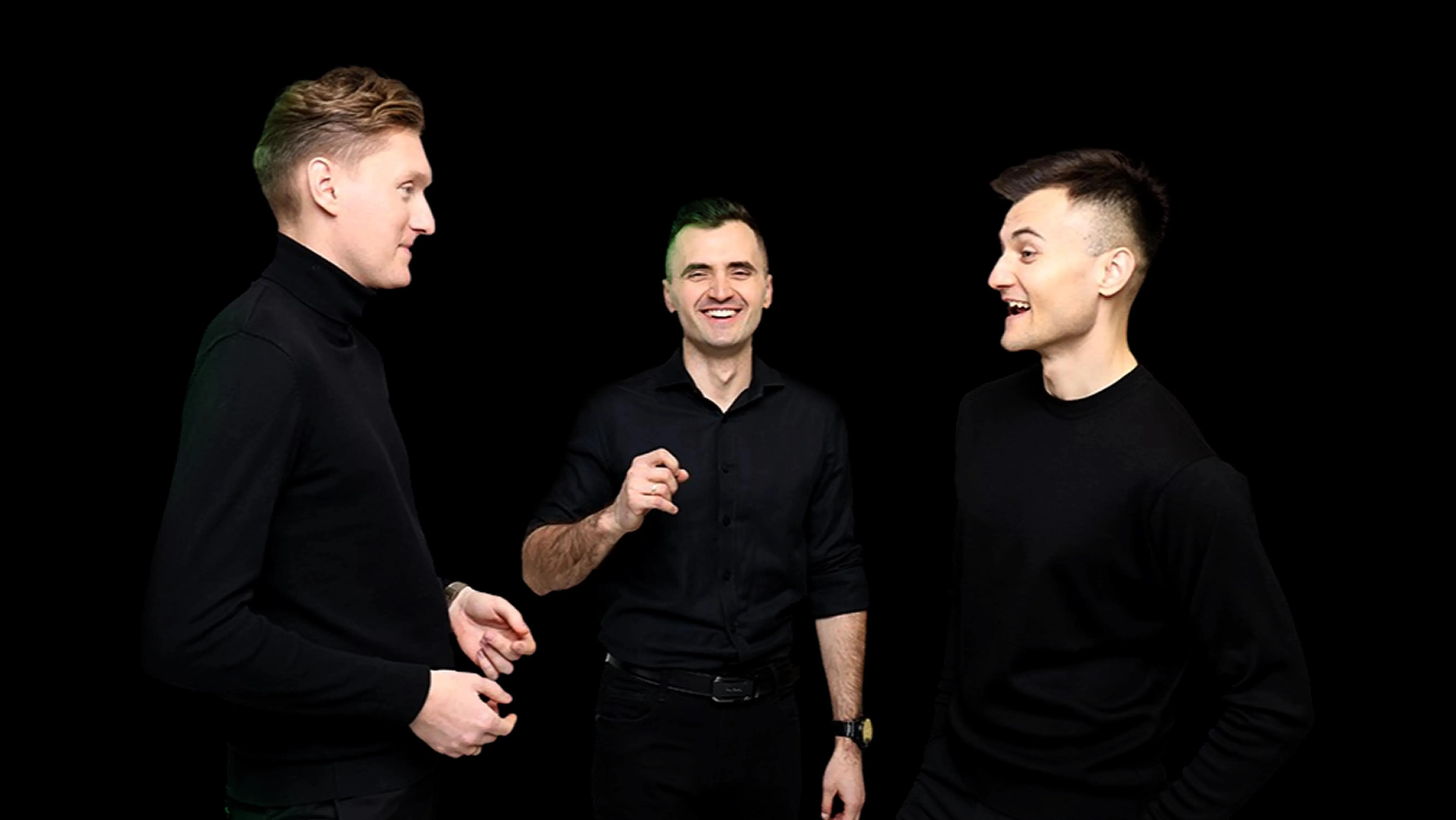 Trzech współpracowników w czarnych golfach śmieje się i gestykuluje, stojąc naprzeciw siebie na czarnym tle.