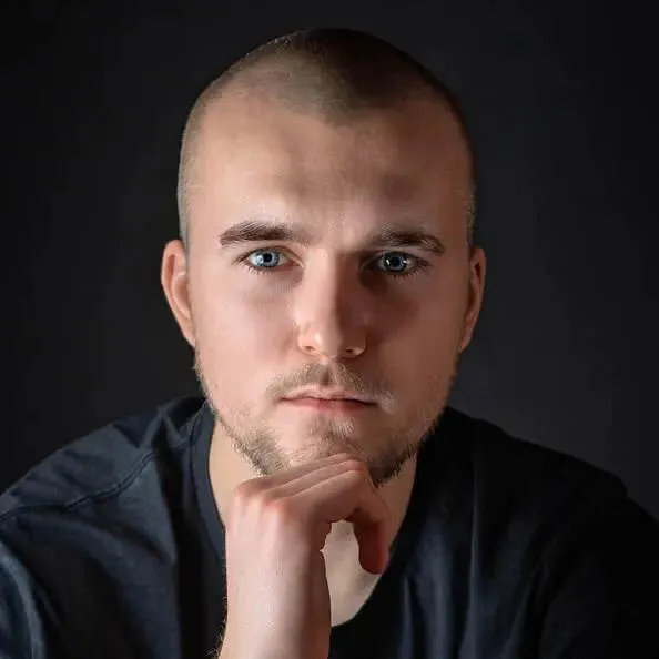 Zbliżony portret Oliwiera z ostrym spojrzeniem, neutralne oświetlenie na szarym tle.