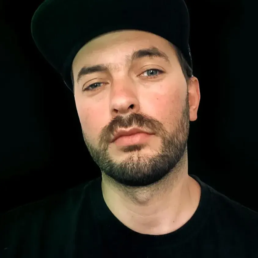 Portret mężczyzny w czapce z daszkiem na ciemnym tle.