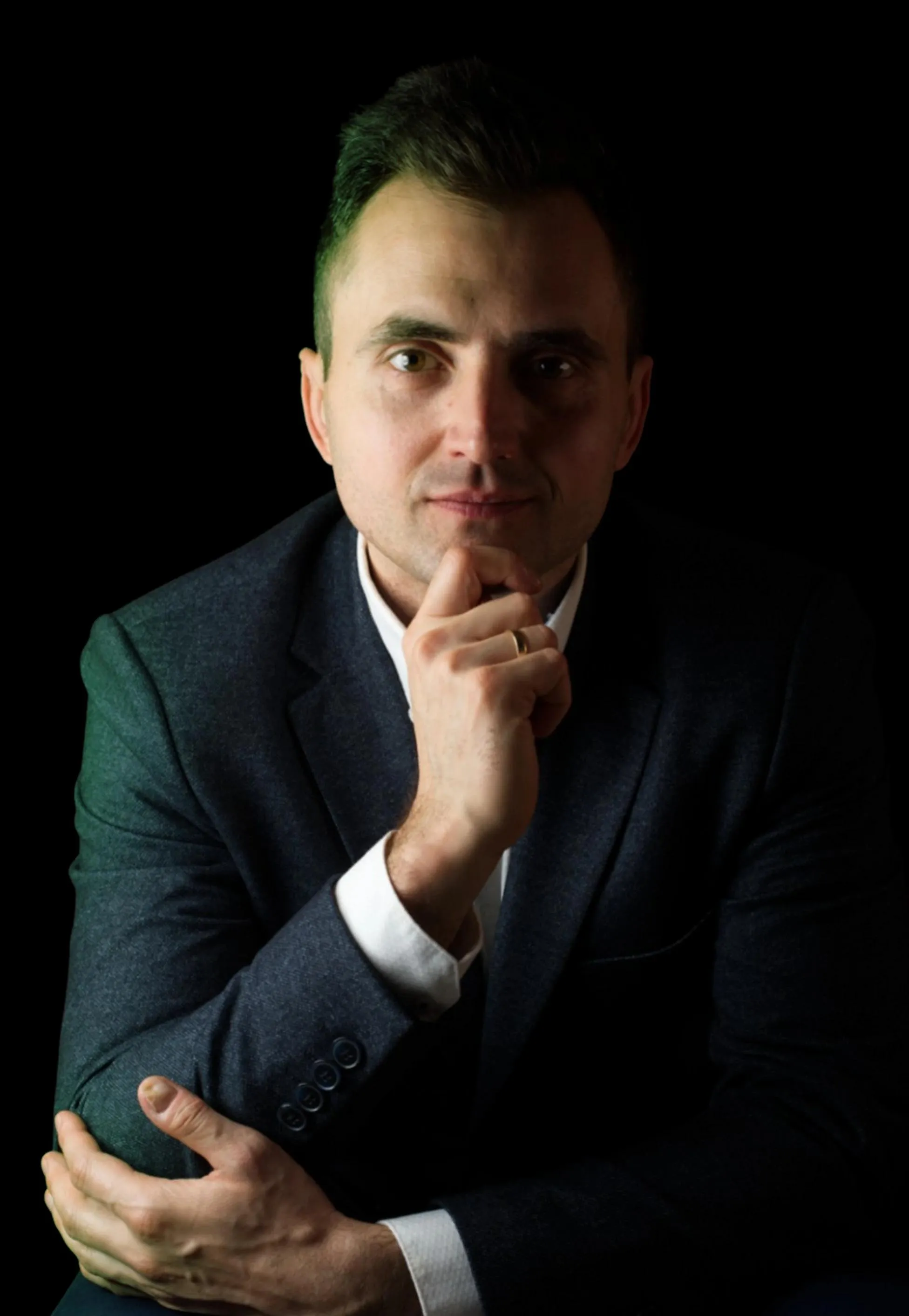 Bliski kadr twarzy Michała opartej na dłoni; ciepłe światło modeluje rysy na czarnym tle.
