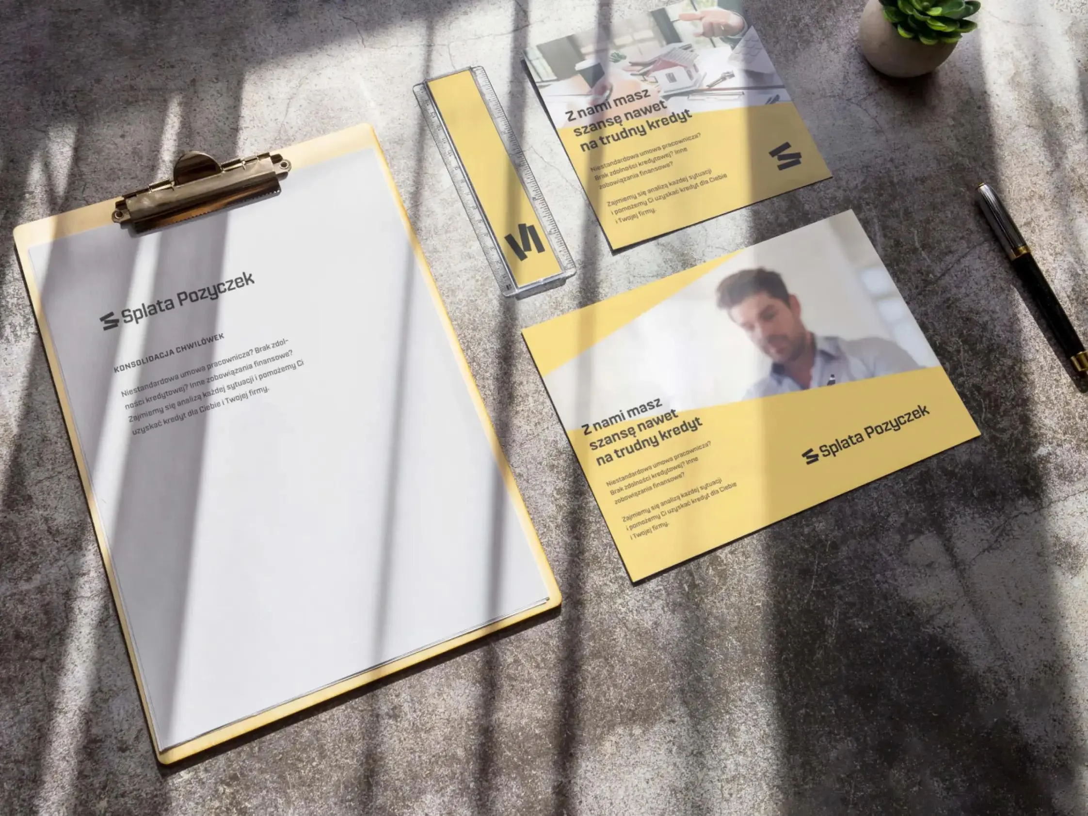 Zestaw materiałów firmowych na biurku: clipboard, wizytówki i ulotka w żółtej palecie.