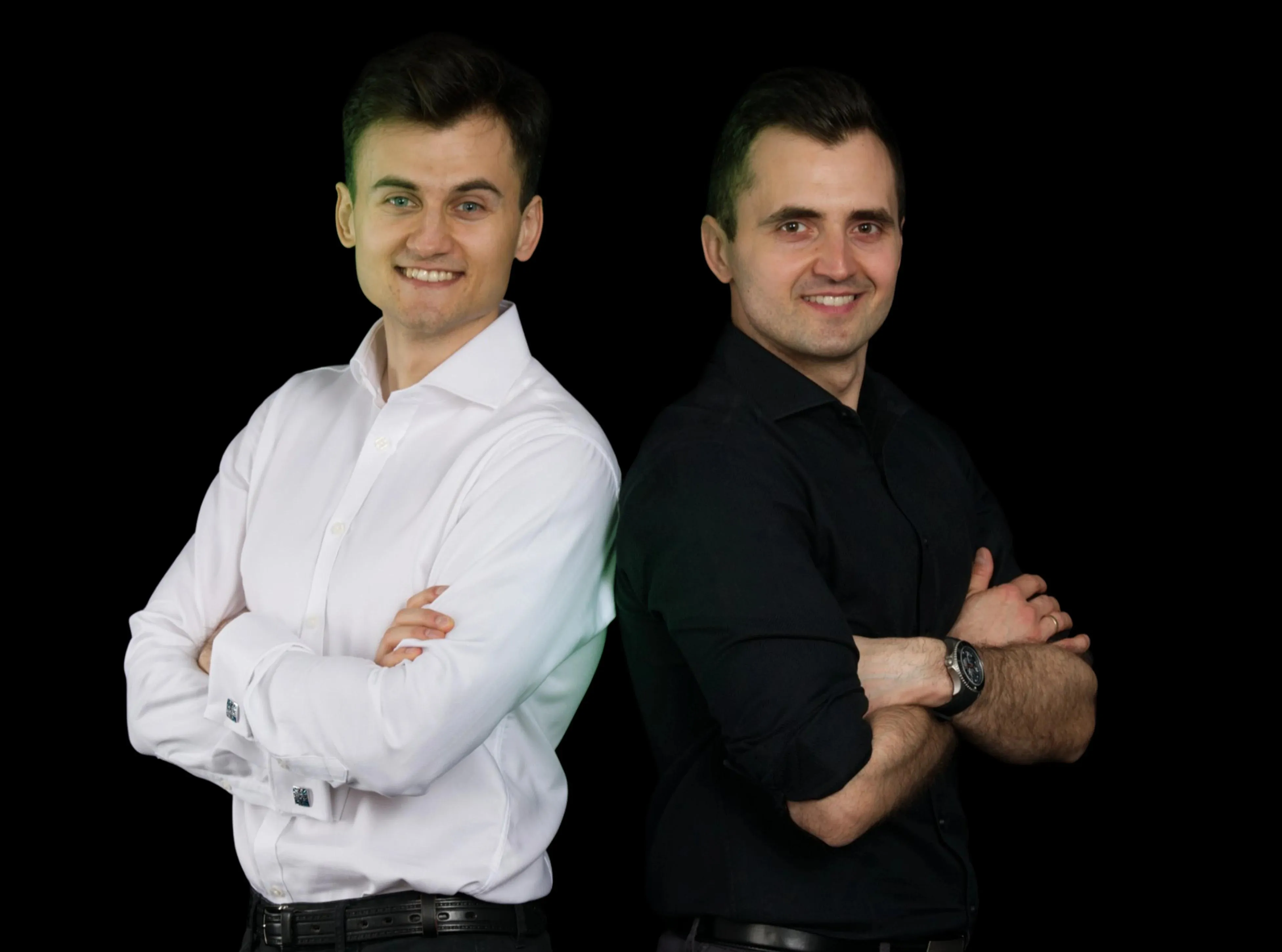 Kuba in a white shirt and Michał in black stand back-to-back, arms crossed and smiling confidently.