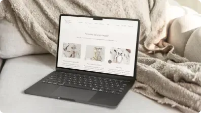 Czarny laptop spoczywa na kremowym kocu i wyświetla stronę z kursami szydełkowania i dziergania marki Kierunek Dzierganie.