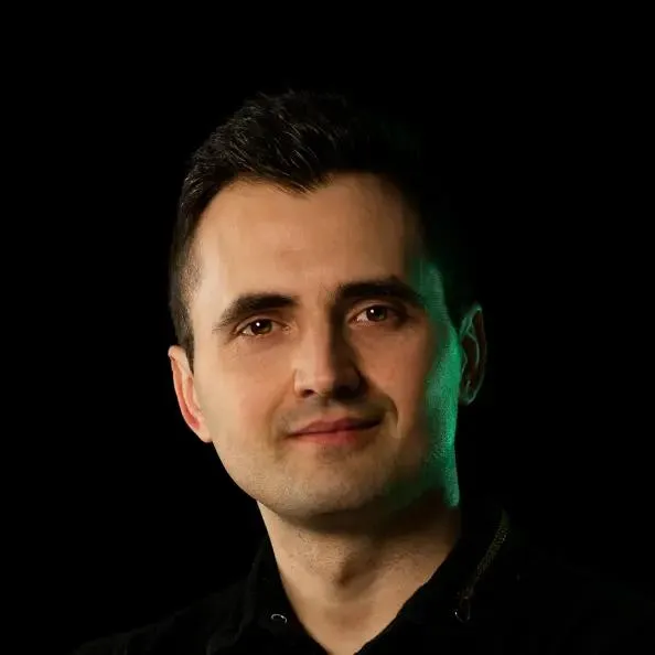 Portrait of Michał on black with a green side rim-light and a calm smile.