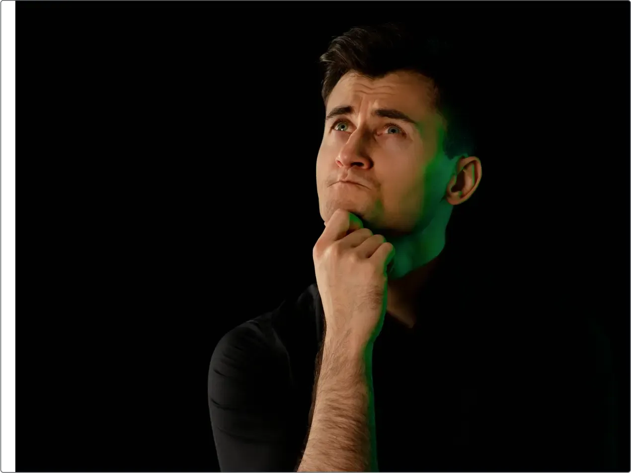 Kuba in a black turtleneck rests his chin on his hand and looks upward against a black background.