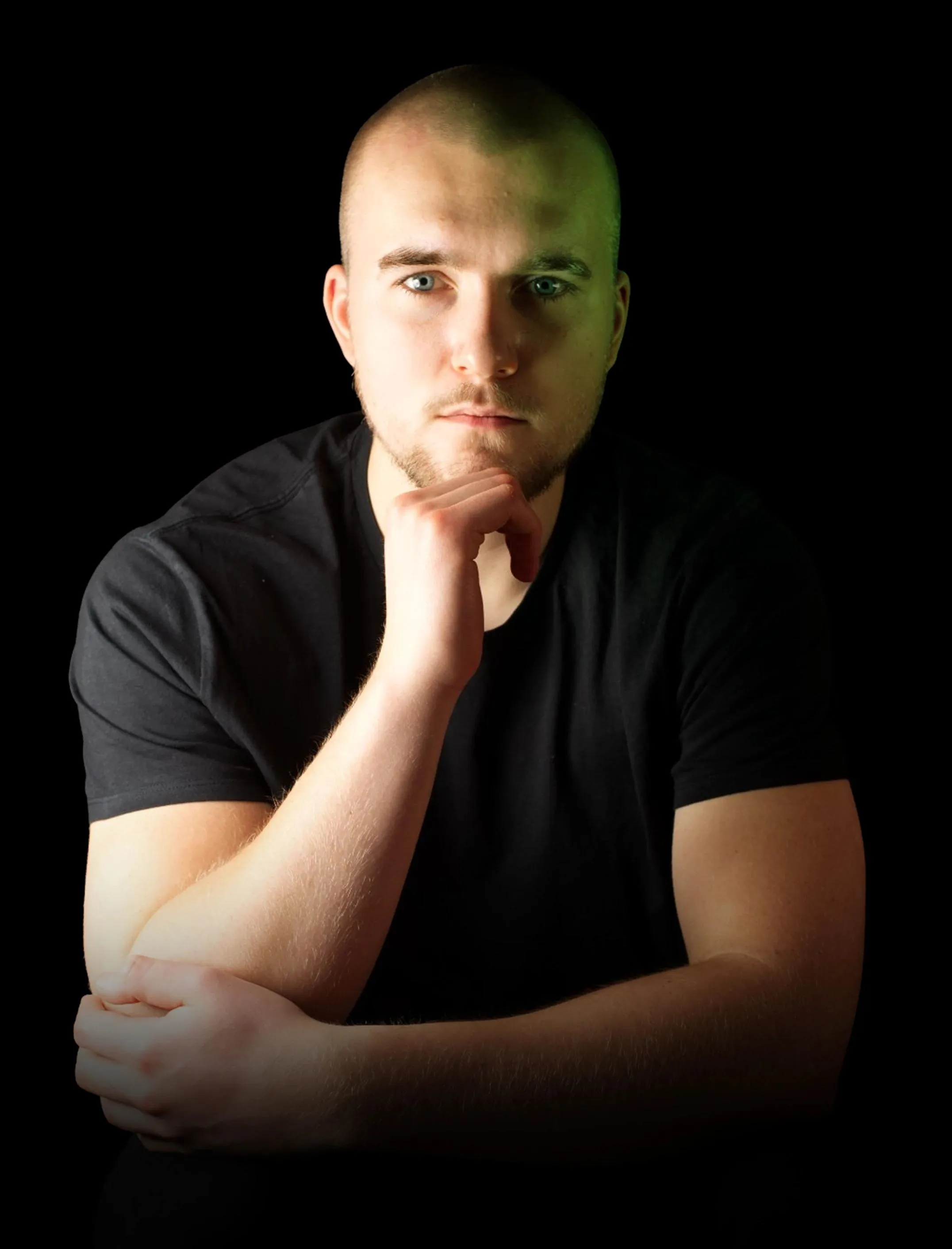Oliwier rests his chin on his fist and looks seriously at the camera; warm light from the left, green light from the right.