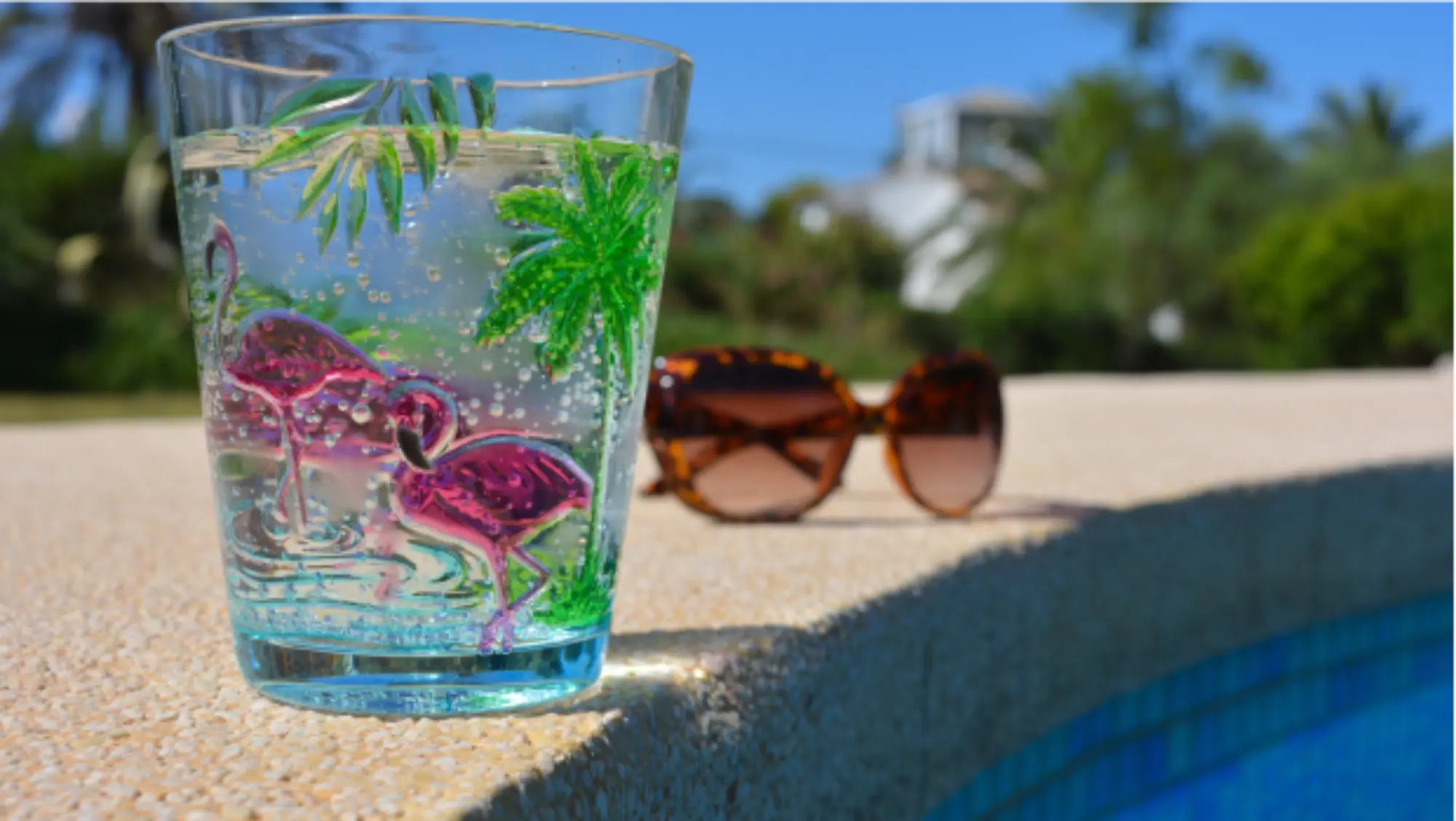Szklanka na brzegu basenu, w tle okulary przeciwsłoneczne